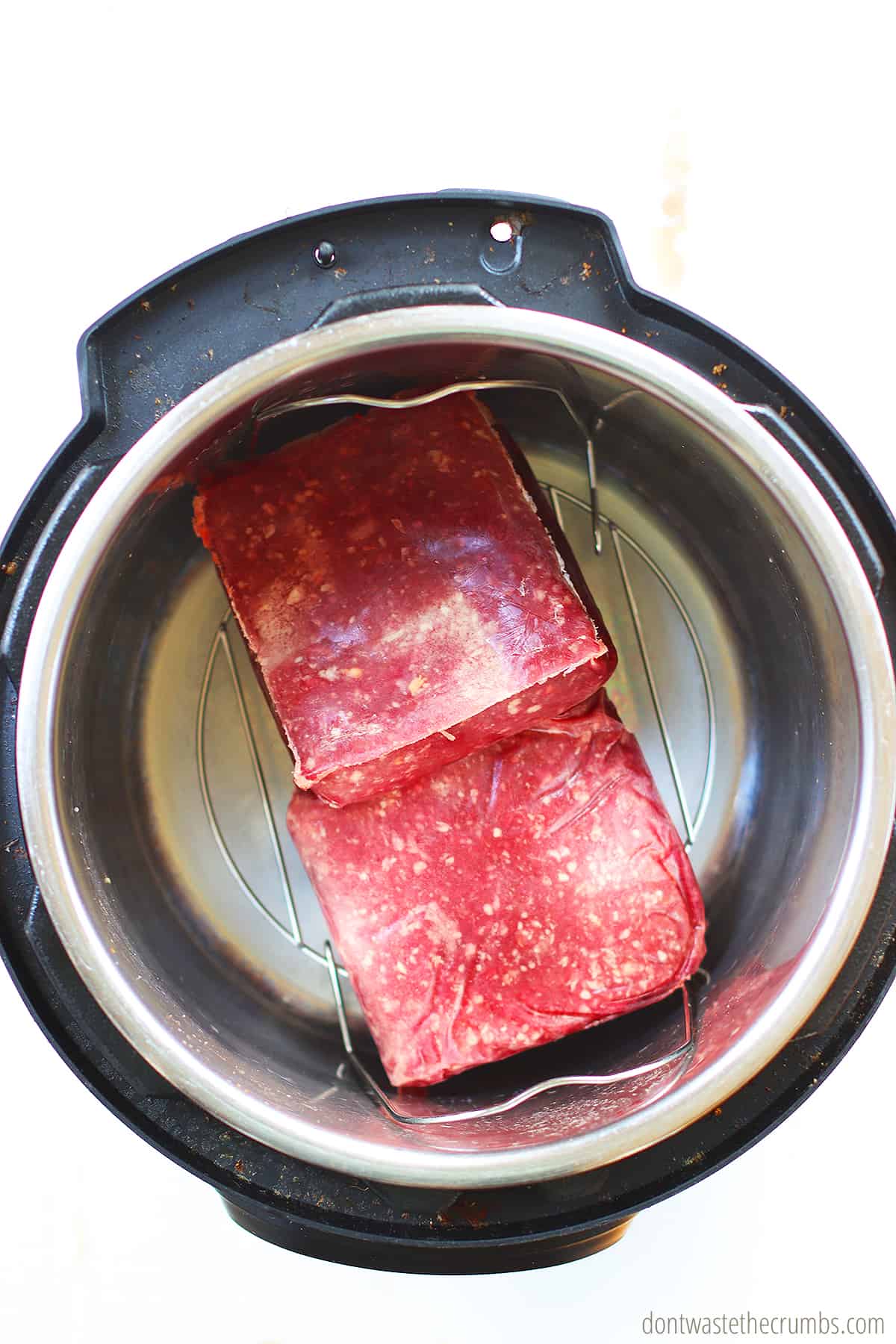 Two pounds of frozen ground beef on a trivet inside of an Instant Pot ready to be cooked. 