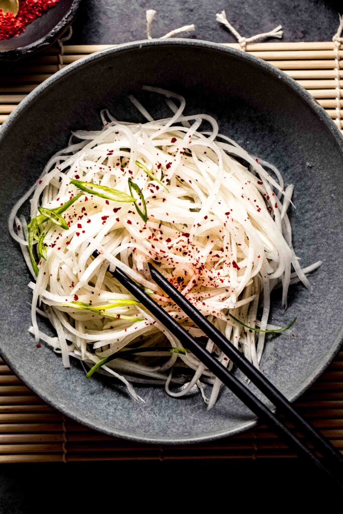 Overhead close up of daikon salad in grey bowl with chopsticks. 