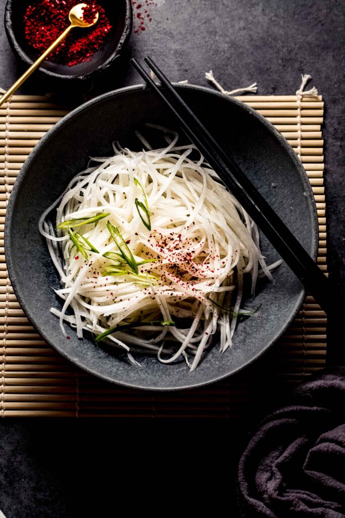 Daikon radish salad in grey bowl sprinkled with red pepper powder. 