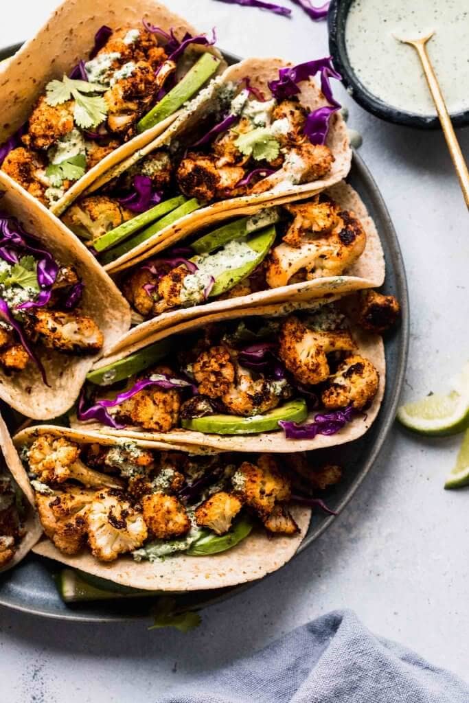 Tacos arranged on plate next to bowl of crema.