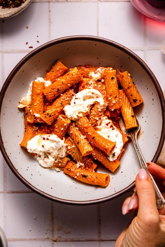 Fork dipping into Smoky tomato pasta with burrata cheese in serving bowl with fork.