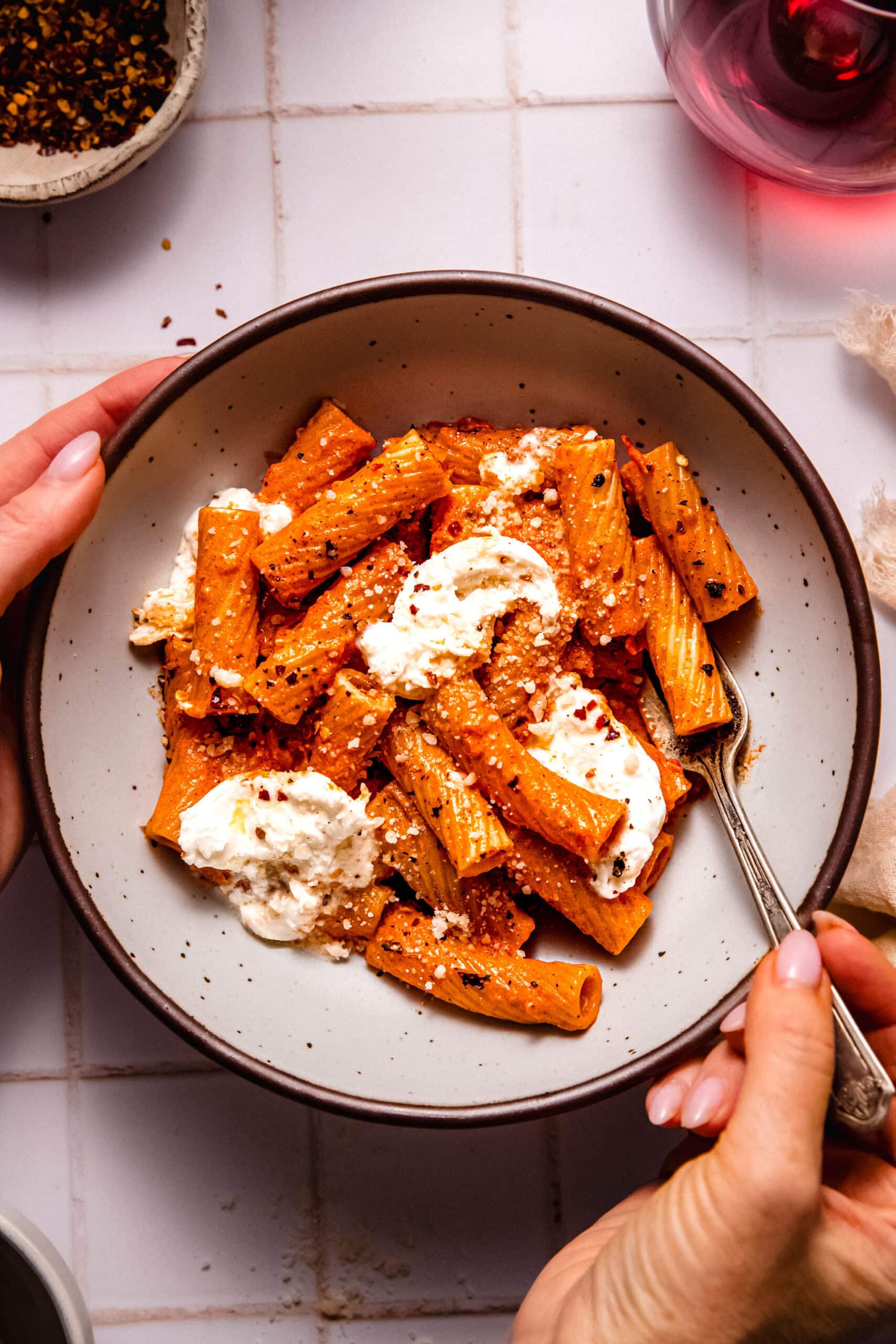 Hands holding bowl of smoky tomato pasta dolloped with burrata cheese.