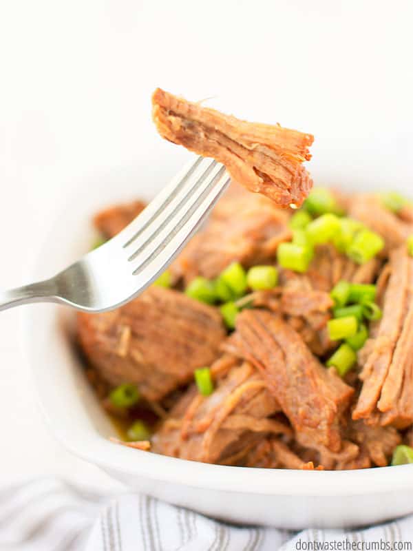 A piece of Korean beef on a fork, with a bowl of Korean beef and green onions below