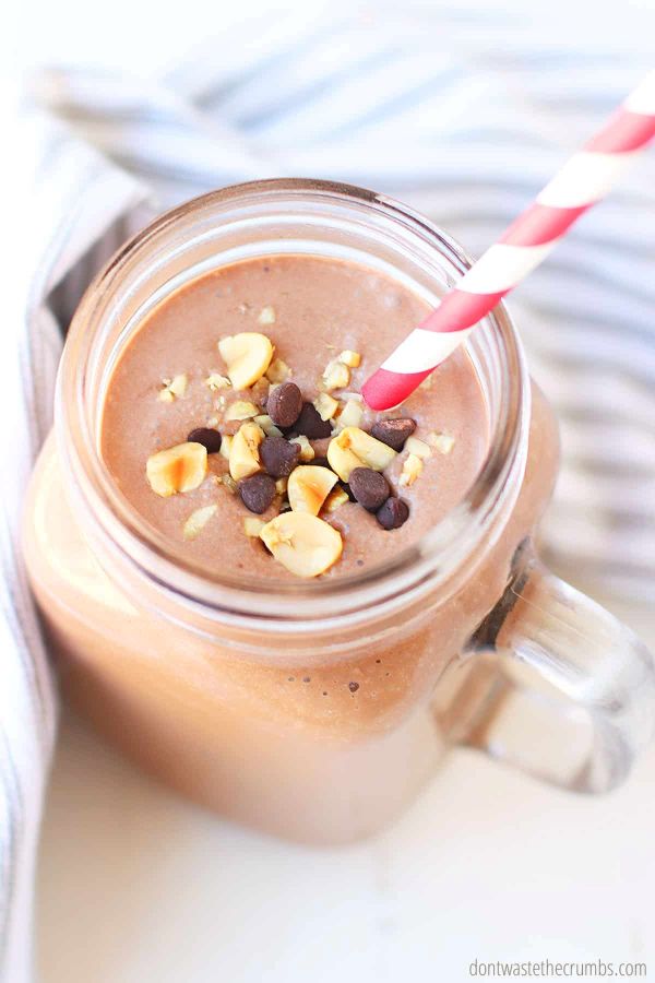 A chocolate peanut butter smoothie with a straw, with chopped peanuts and chocolate chips sprinkled on top.
