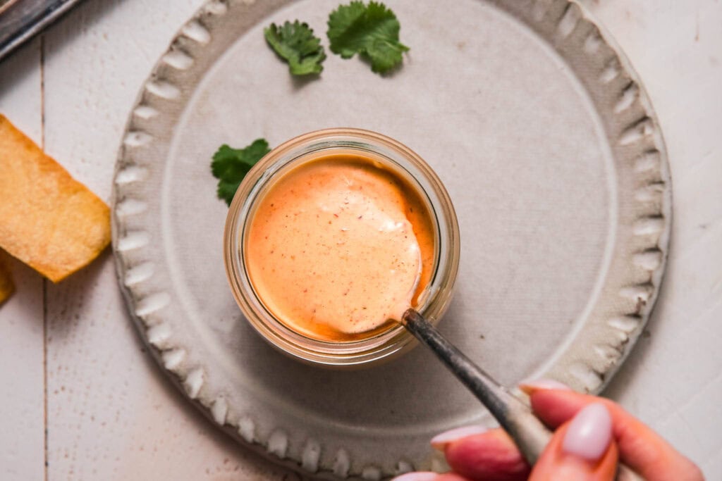 Overhead shot of hand stirring jar of southwest ranch dressing. 